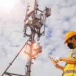 un tecnico con dispositivi di sicurezza e mascherina controlla una grande antenna con un dispositivo elettronico