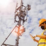 un tecnico con dispositivi di sicurezza e mascherina controlla una grande antenna con un dispositivo elettronico